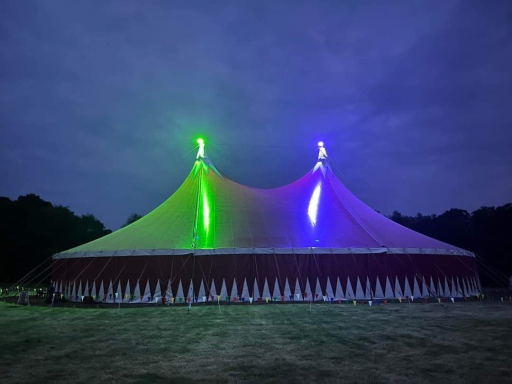 A big top tent lit up in blue and green against the night sky