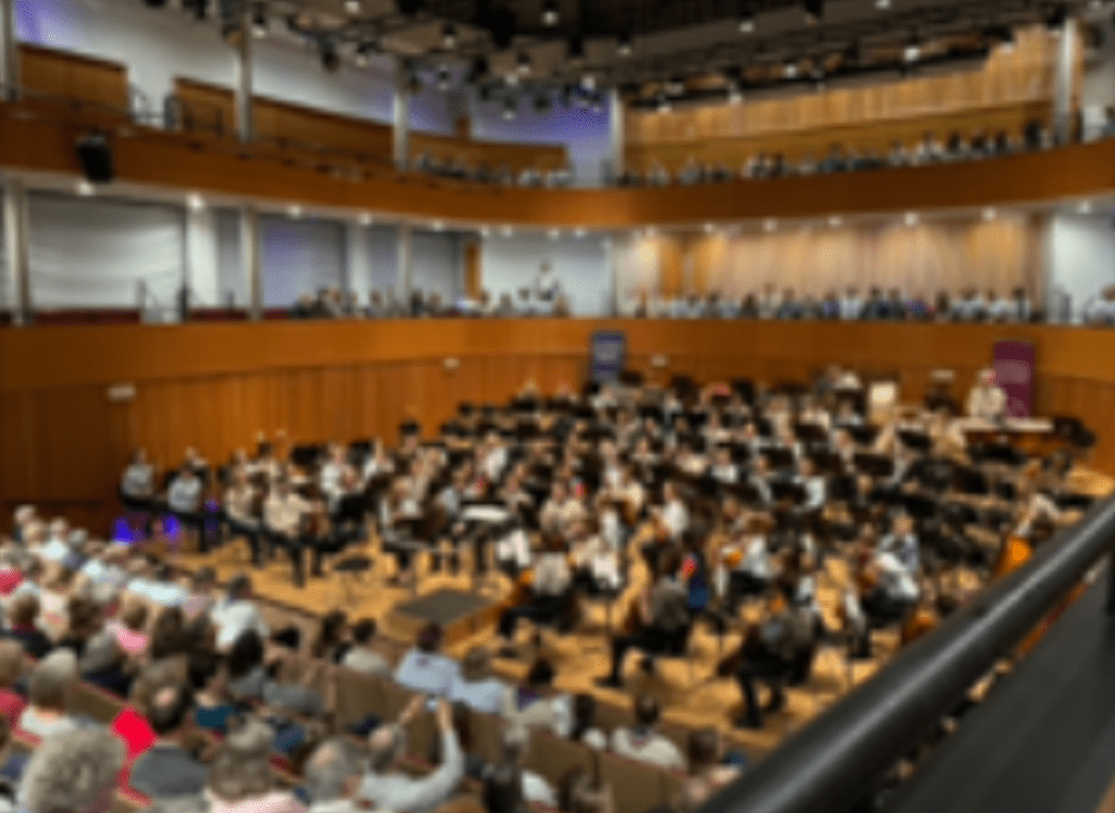 Guide and Scout musicians playing with their orchestra in their concert, with an audience looking on.