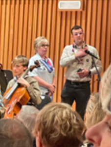 A photo of a woman, the Chief Guide, and a man, the Scout UK Commissioner for Programme, in uniform, with young people in the foreground getting ready to play