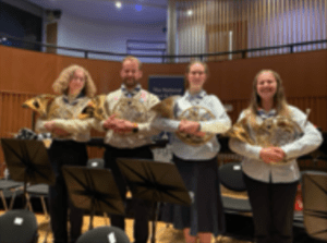 Four young people in guide and scout uniforms holding their french horns