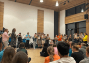 A large group of young people in watch while others stand in front and play brass instruments