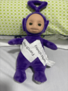 The purple tellytubby, Tinky Winky, resting against a green pillow