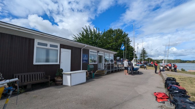 Photo in front of Durleigh Sailing Centre clubhouse with a bright blue sky and boats being rigged close to the reservoir.